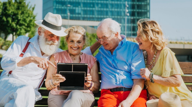Zdjęcie seniorów siedzących na ławeczce z laptopem
